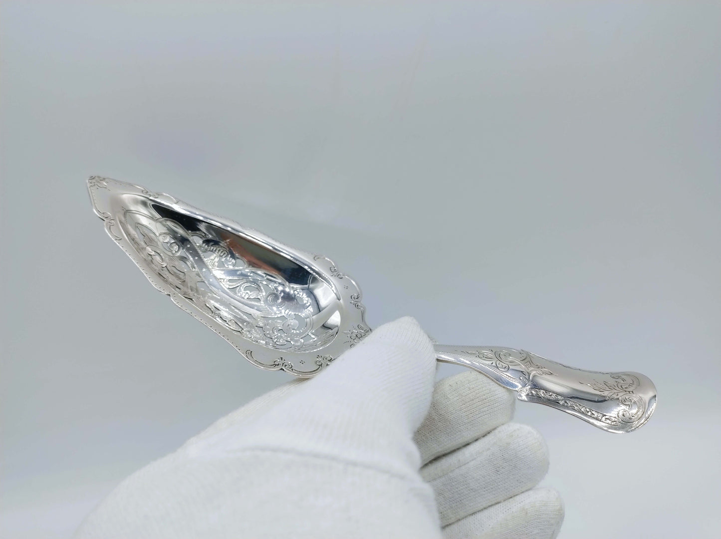 Zilveren natfruitschep vastgehouden met witte handschoen, ovale bak in beeld
