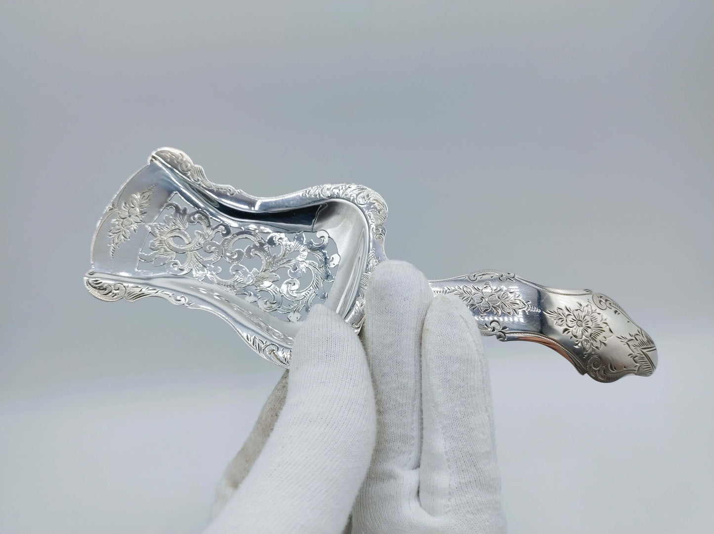 Zilveren natfruitschep vastgehouden met handschoen, met gegraveerd ornament