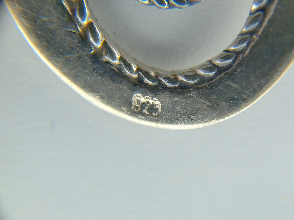 Close-up van zilveren oorbel met gegraveerde markering aan de achterkant.
