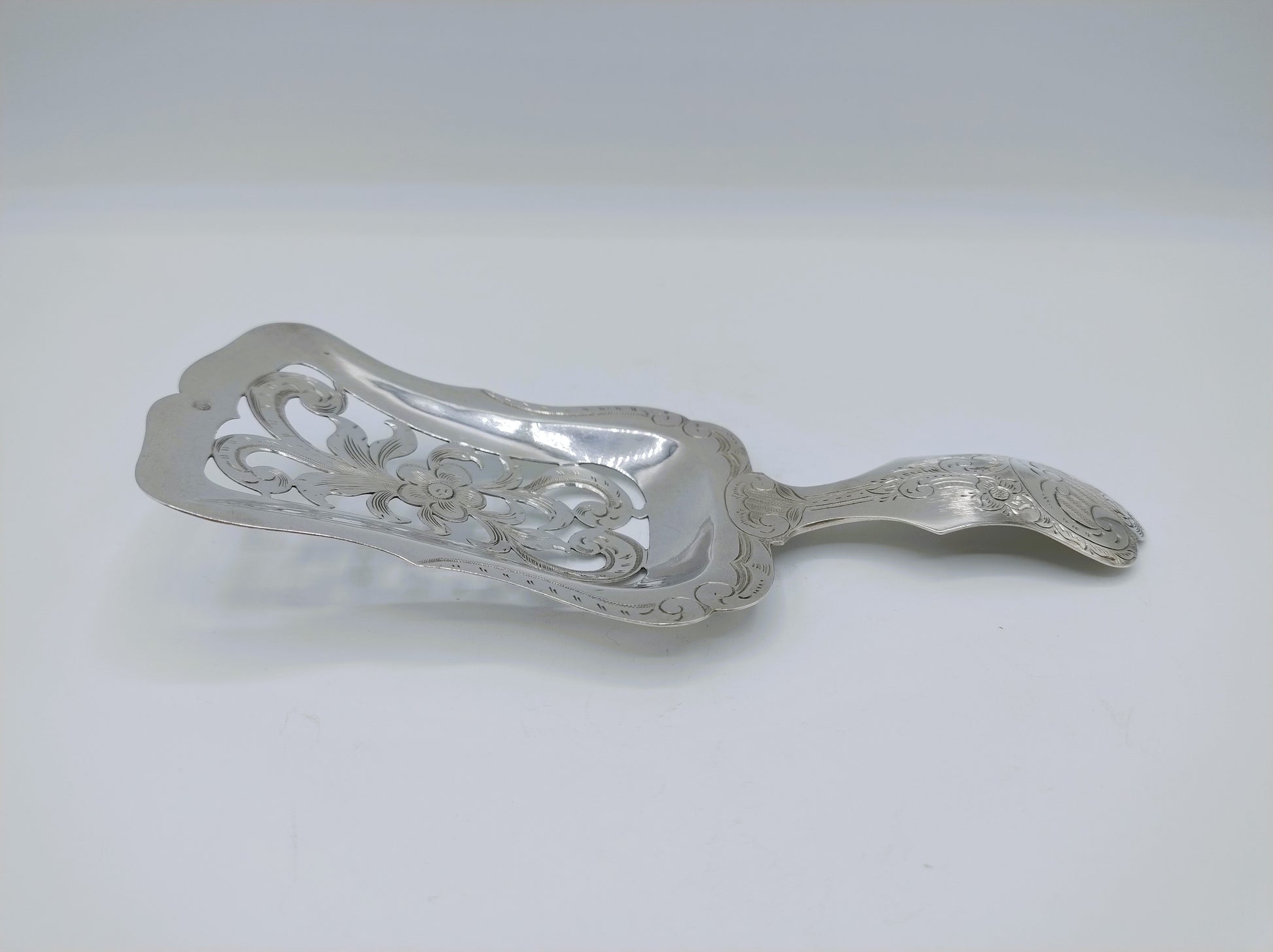 Zilveren natfruitschep in profiel met decoratieve rand en gebogen steel, glanzend