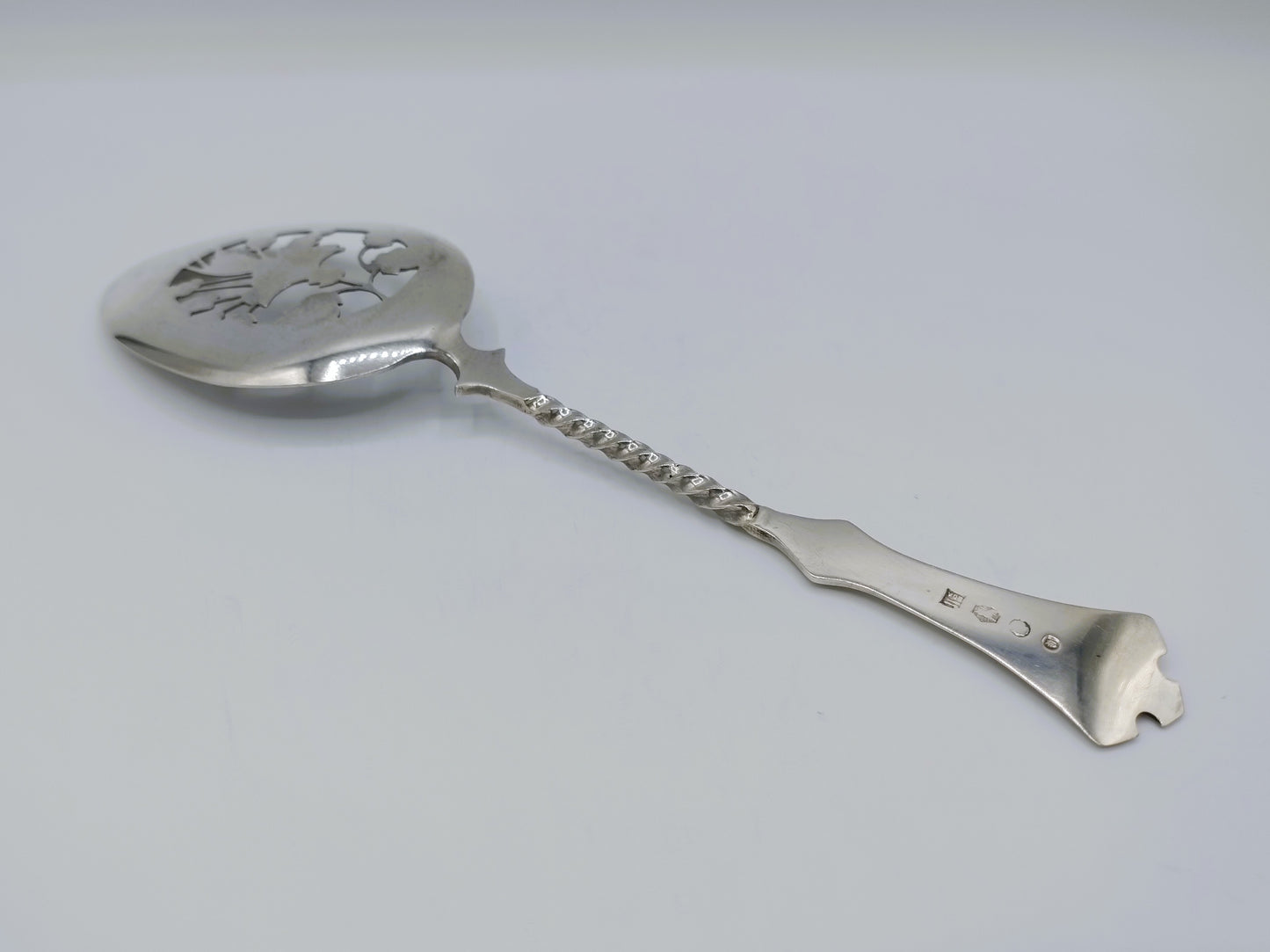 Zilveren natfruitschep met gegraveerd bloemmotief op lepelbak en gedraaide steel