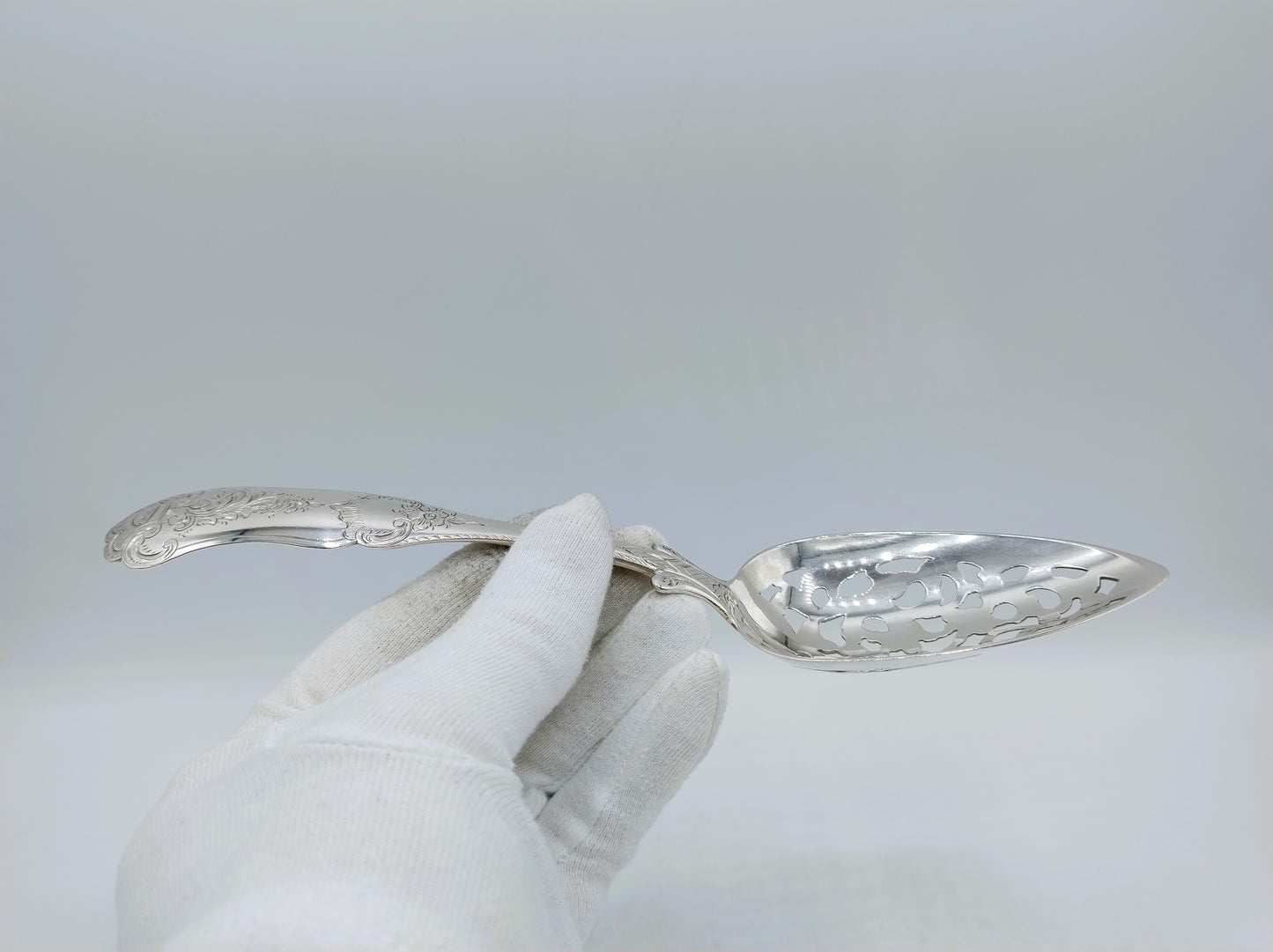 Zilveren natfruitschep vastgehouden; gegraveerde lepel en slanke steel