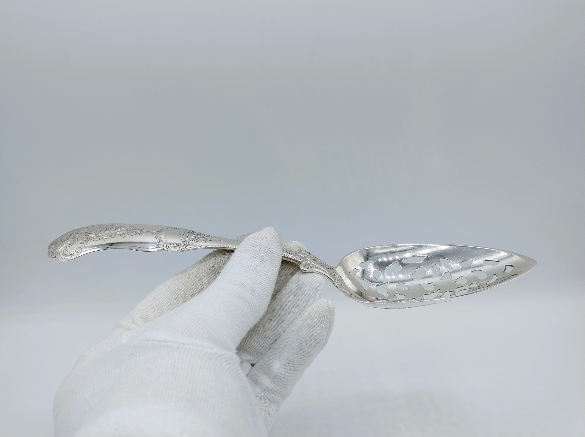 Zilveren natfruitschep vastgehouden; gegraveerde lepel en slanke steel