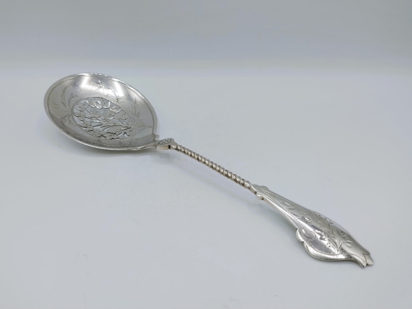Zilveren natfruitschep met ronde lepel, kettingsteel en gegraveerde decoratie op de kom.