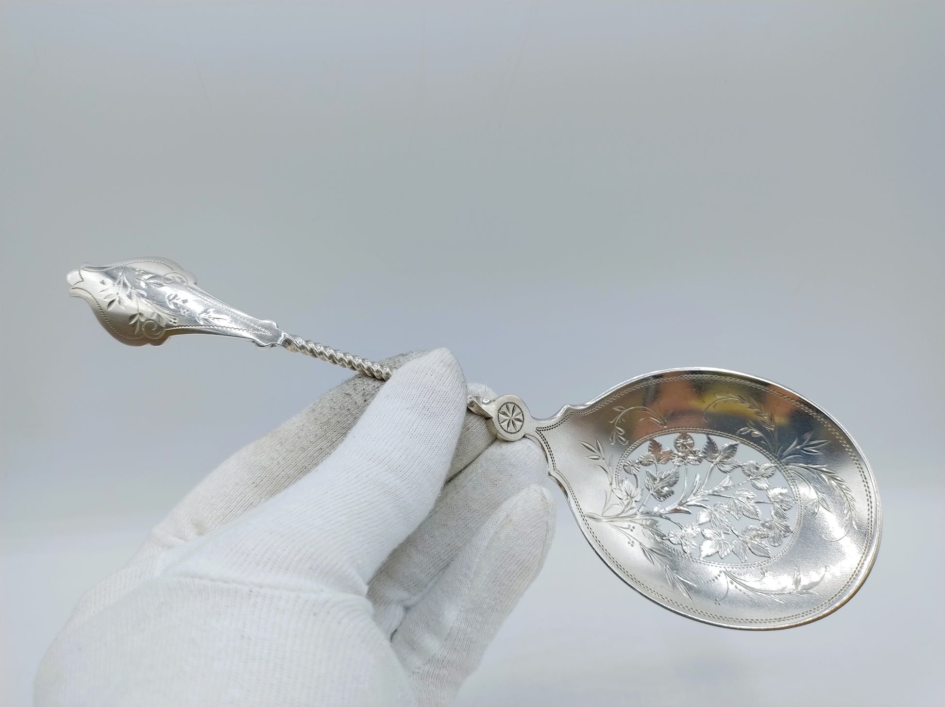 Zilveren natfruitschep vastgehouden met handschoen; ovale kom met sierlijke gravure.
