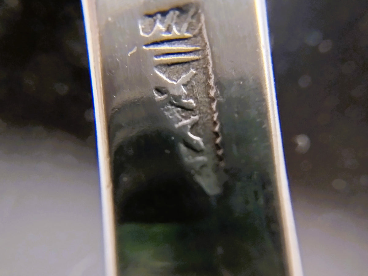 Stempel met reliëfletters op zilveren metalen onderdeel.