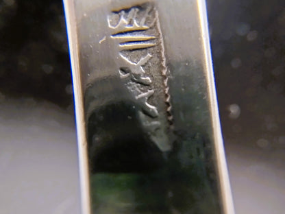 Stempel met reliëfletters op zilveren metalen onderdeel.