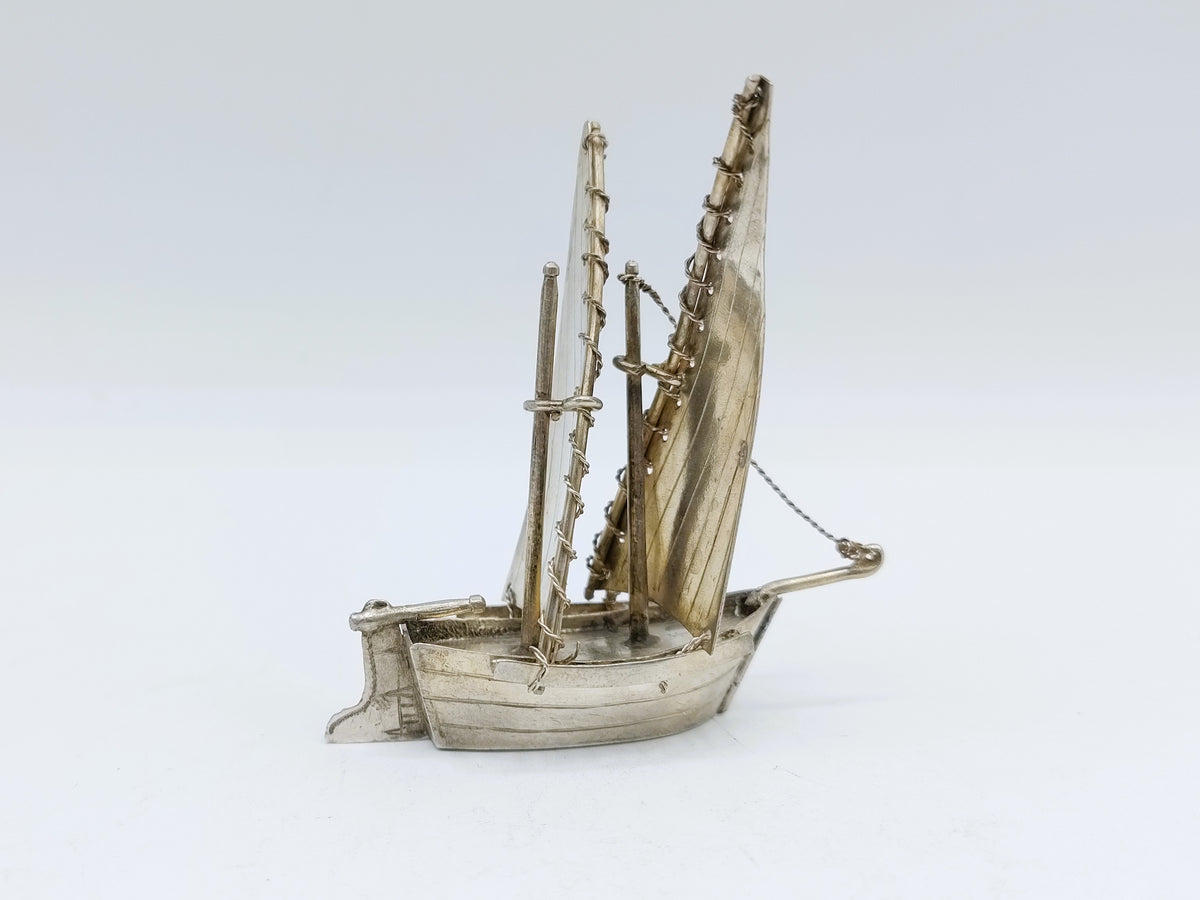 Zilveren miniatuurzeilschip met zeilen en masten, op liggende romp