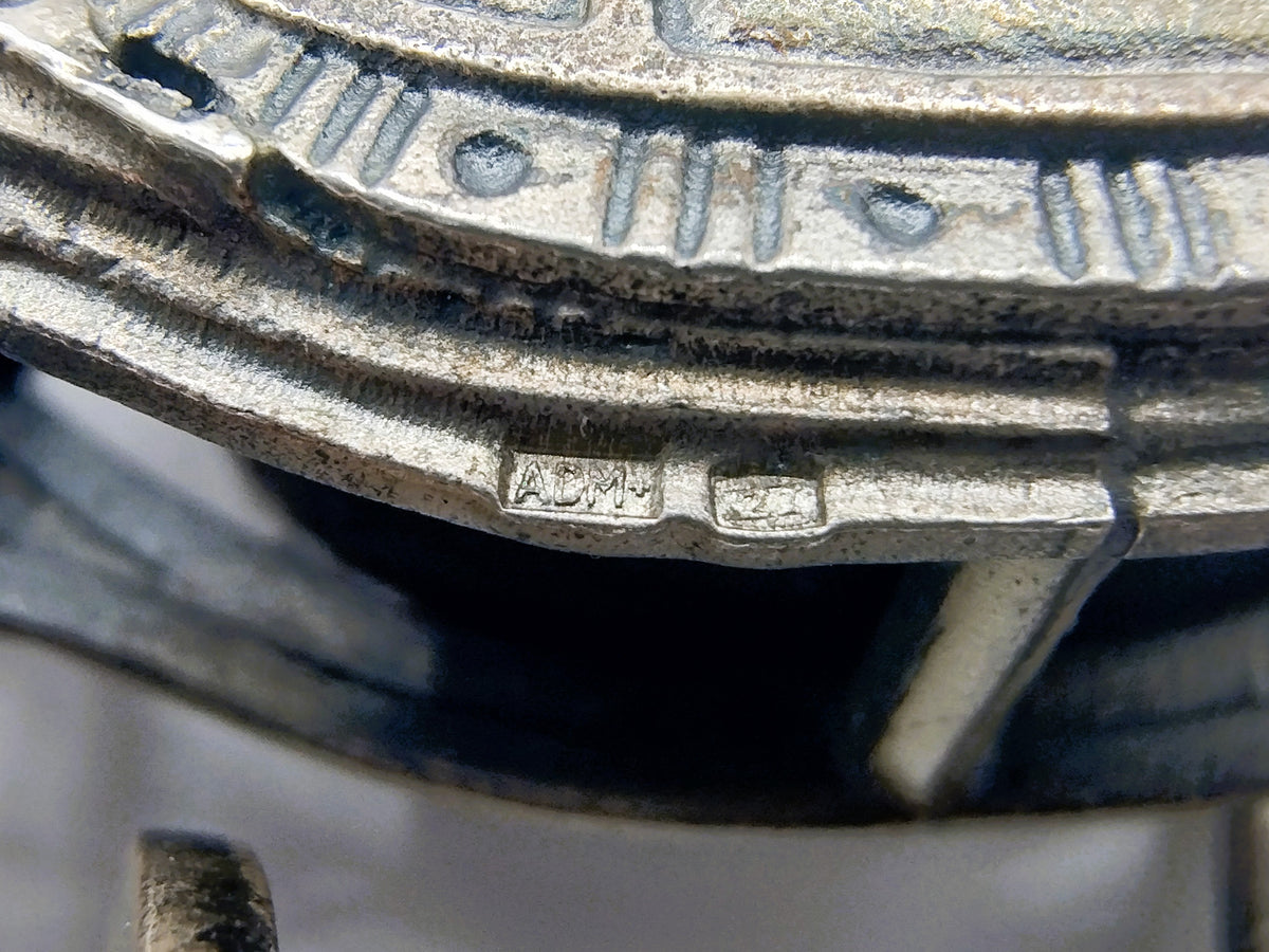 Onderdeel van zilverkleurige miniatuurkoets met gegraveerde tekst en merkteken