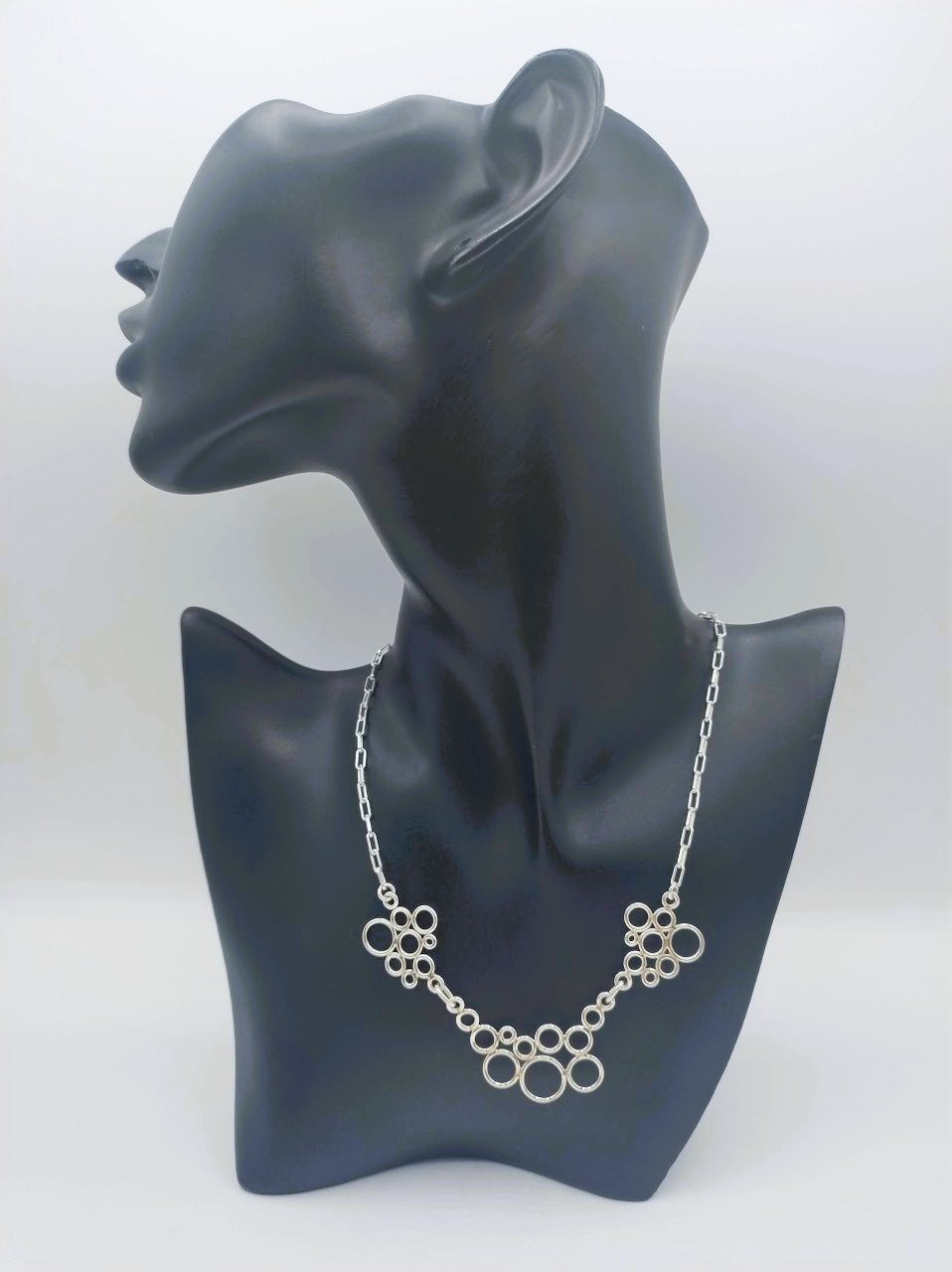 Zilveren ketting met decoratieve ringen, hangt bij de hals op paspop