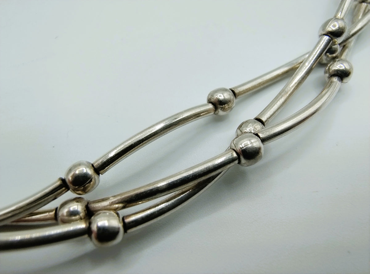 Zilveren kettingdetail: staafschakels met bolvormige klemmetjes en ringverbinding.