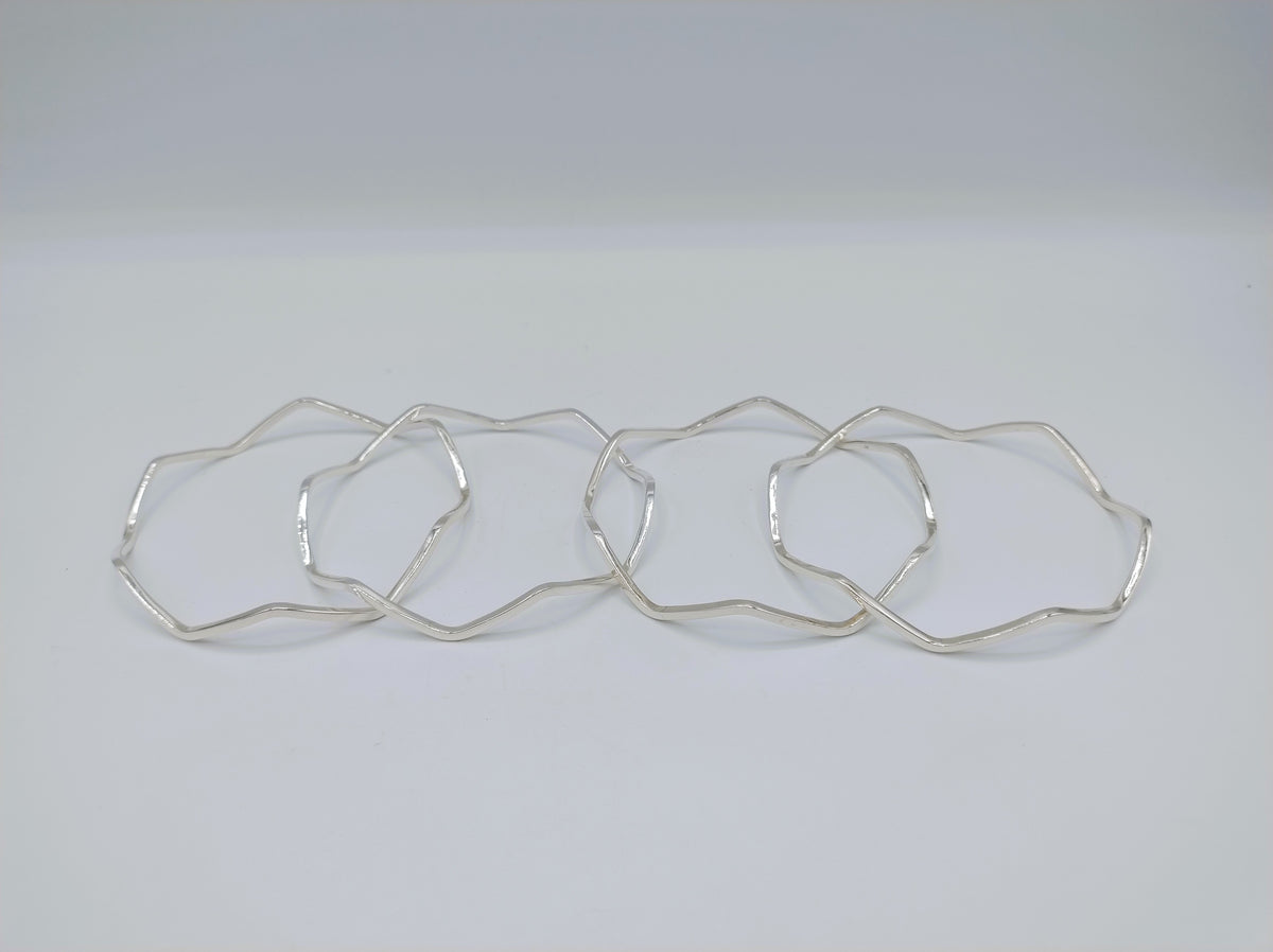 Vier zilverkleurige armbanden met stervormige, golvende schakels, plat gelegd
