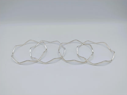 Vier zilverkleurige armbanden met stervormige, golvende schakels, plat gelegd
