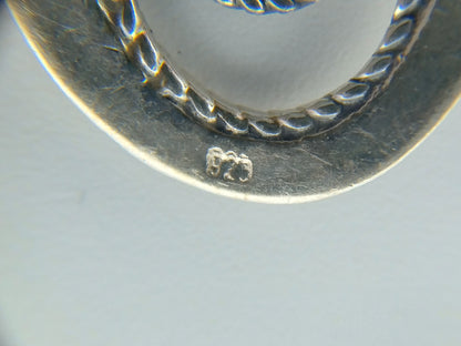 Close-up van zilveren oorbel met gegraveerde markering aan de achterkant.