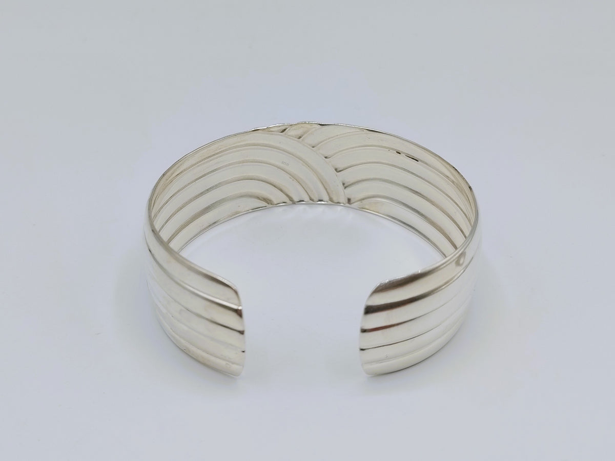 Zilveren cuff armband met golfmotief; afgeronde uiteinden en gestreepte structuur.