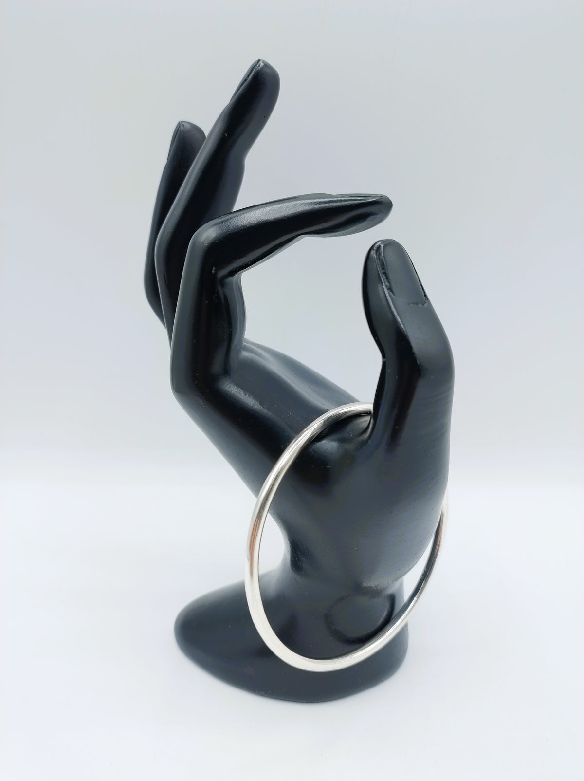 Zilveren slavenarmband met open ovale ring, opgestoken op een hand