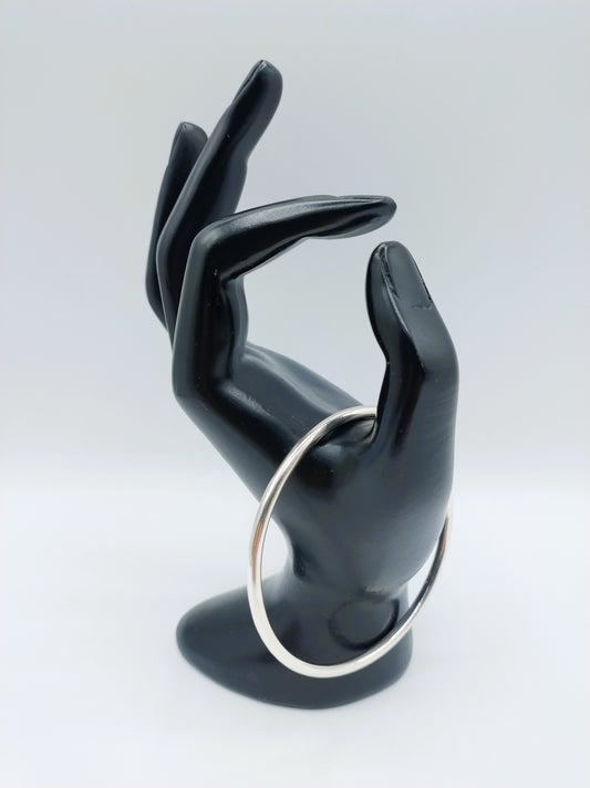 Zilveren slavenarmband met open ovale ring, opgestoken op een hand