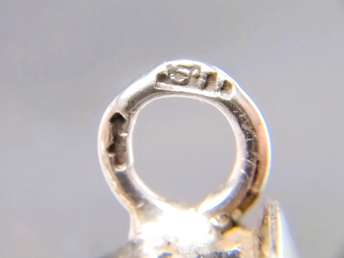 Close-up van zilveren breipendop-lus met ingeslagen stempelmarkering