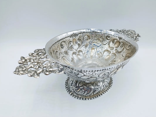 Zilveren brandewijnkom met rijk gegraveerde ornamenten en twee decoratieve handvatten
