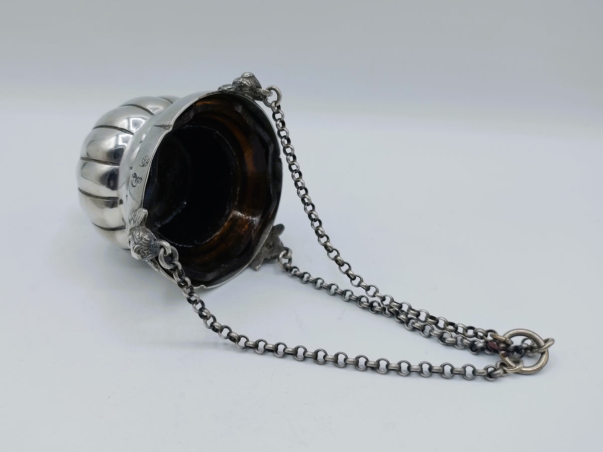 Zilveren altaarlamp met ketting en donker glas in metalen houder.