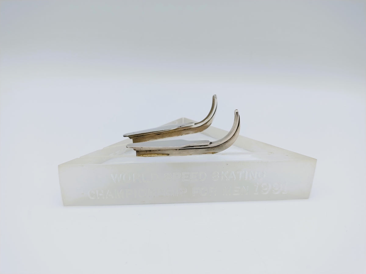 Zilveren schaatsenmemorabilia met twee metalen blades op witte blokvoet met inscriptie.