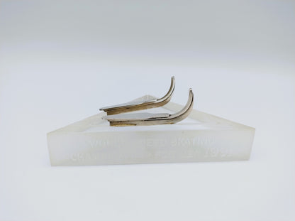 Zilveren schaatsenmemorabilia met twee metalen blades op witte blokvoet met inscriptie.