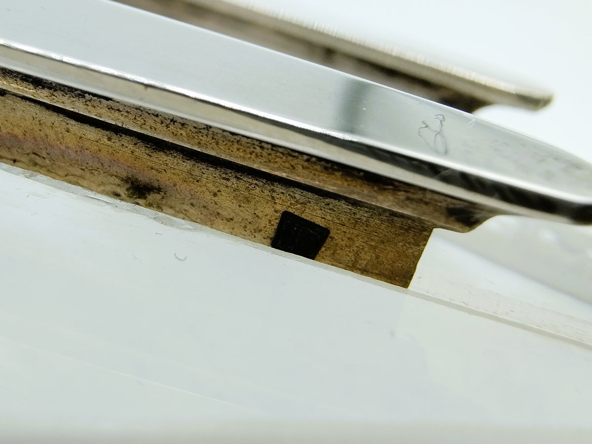 Detail van zilveren randen en metalen voet op witte basis, zwarte inzet zichtbaar.