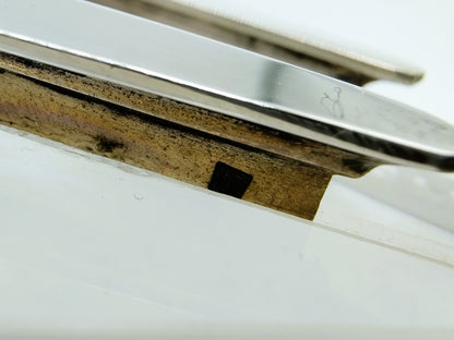 Detail van zilveren randen en metalen voet op witte basis, zwarte inzet zichtbaar.