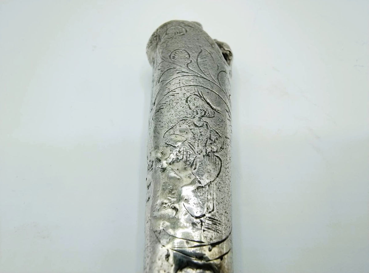 Close-up van zilveren heft met reliëfgravure van een gezicht en ornamenten.