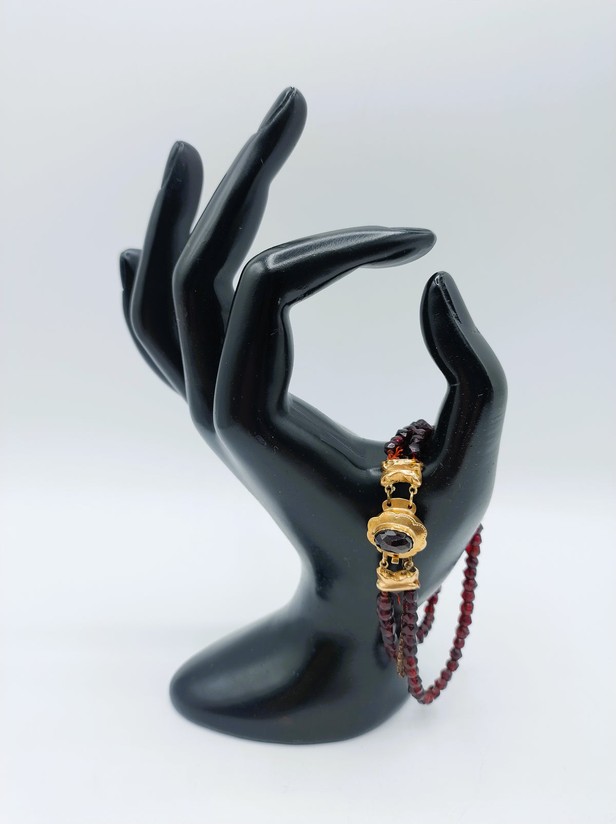Glasgranaten armband met gouden slot op zwarte mannequinhand, met rode kralen