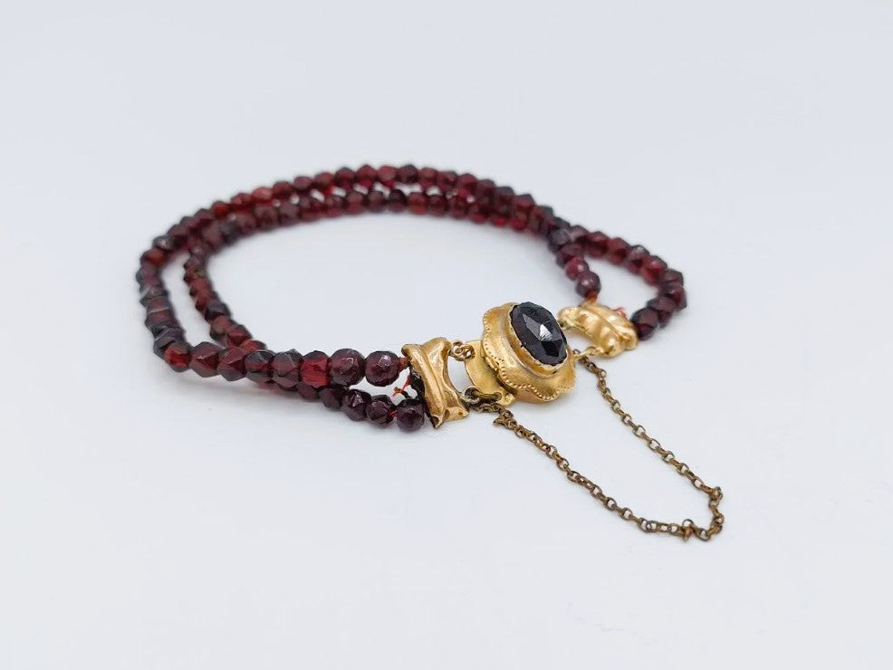 Glasgranaten armband met rode kralen, goudkleurige beugel en zwarte steen met kettinkje
