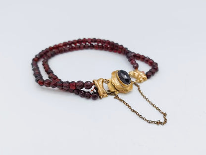 Glasgranaten armband met rode kralen, goudkleurige beugel en zwarte steen met kettinkje