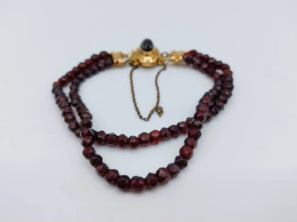 Platliggende glasgranaten armband met rode facetranden en goudkleurige sluitdetails