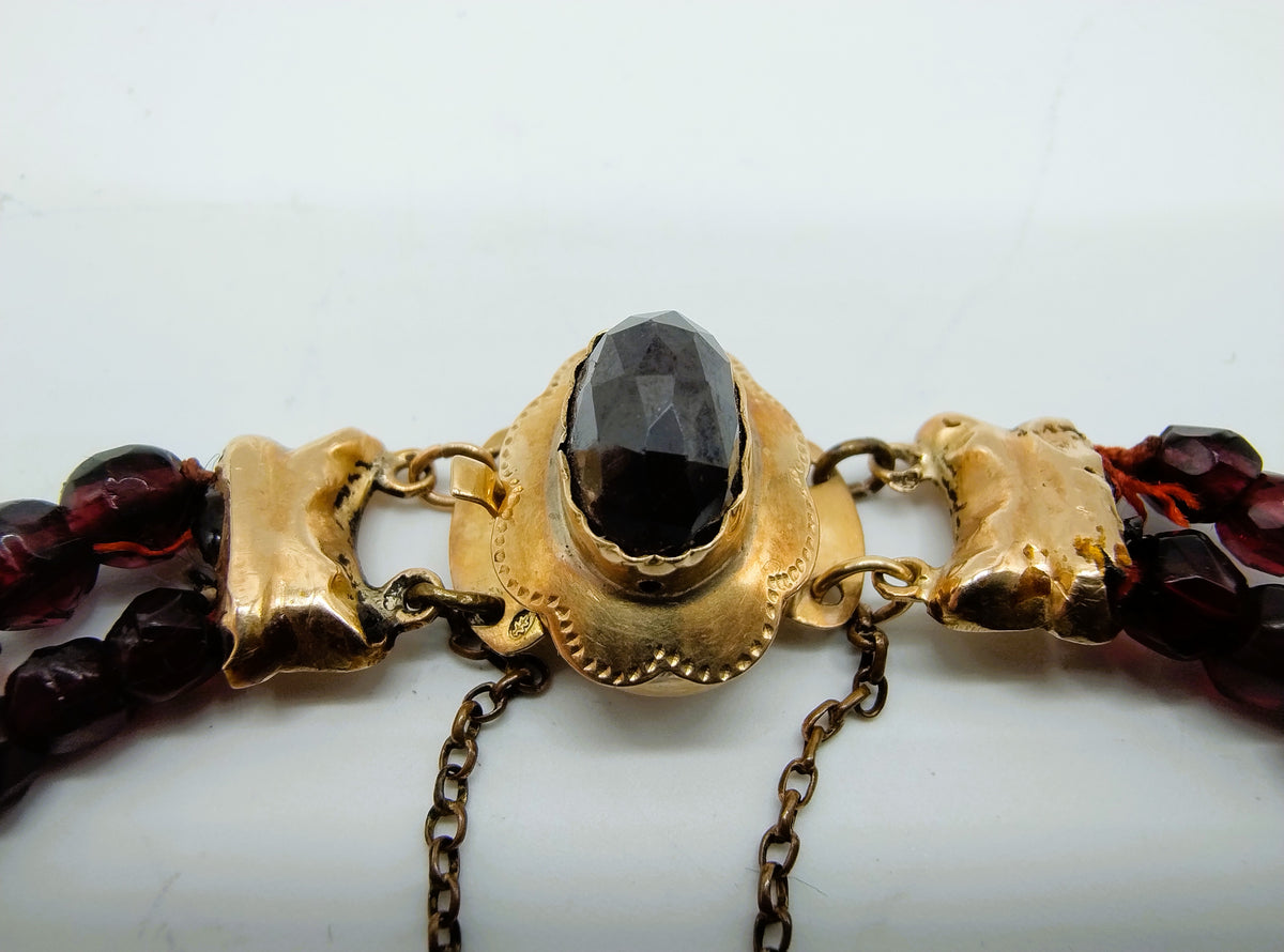 Detail van glasgranaten armband: goudkleurige setting met zwarte steen en rode kralen
