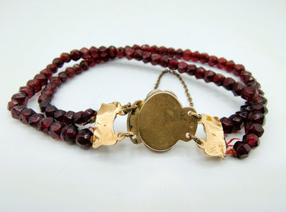 Glasgranaten armband met rode kralen en goudkleurige ronde sluitplaat met ketting