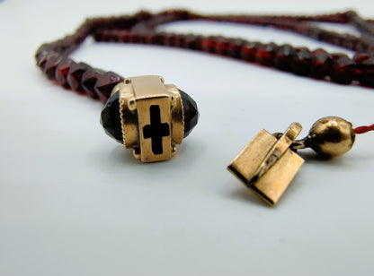 Einde van de ketting: gouden dop met ingegraveerd kruis, met bordeauxrode kralen.