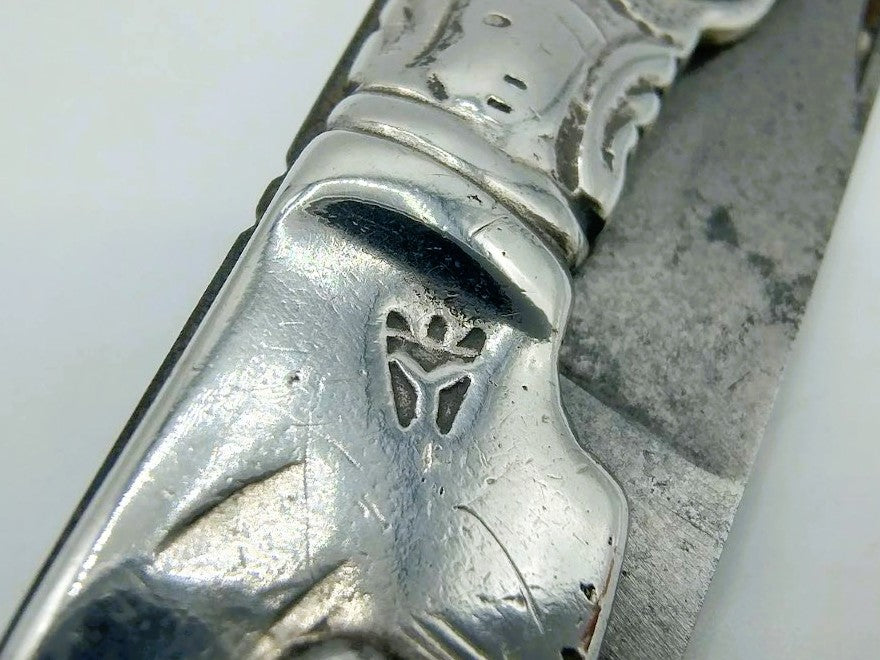 Close-up van zilveren zakmes met reliëfdecor op het heft en rand van lemmet