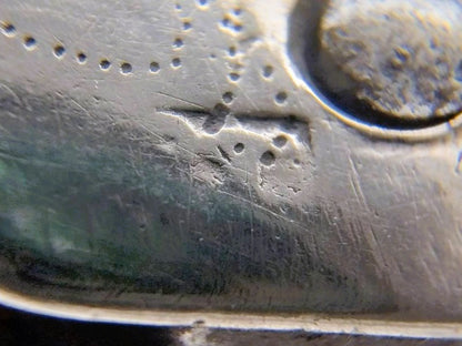 Close-up gravure op zilveren heft met stempelwerk en kleine beschadigingen