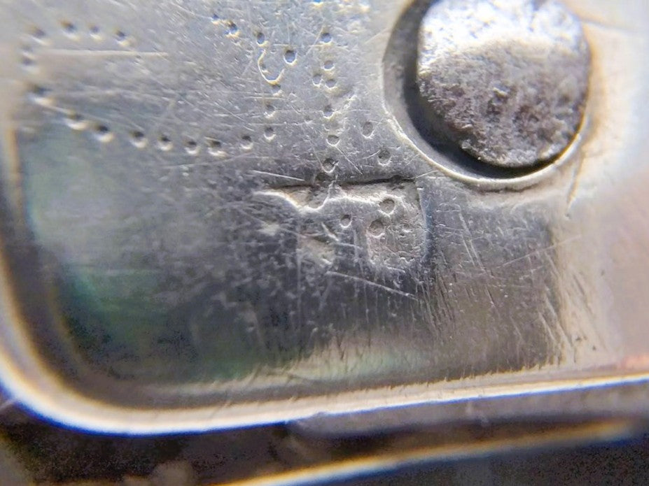 Close-up van zilveren heft met reliëf en ronde markering naast decoratieve lijnen