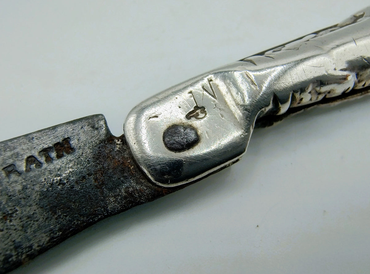 Zilveren zakmesheft met gegraveerd patroon en rond embleem op het zilver