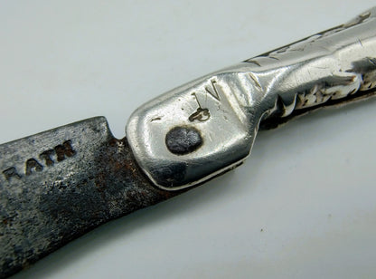 Zilveren zakmesheft met gegraveerd patroon en rond embleem op het zilver