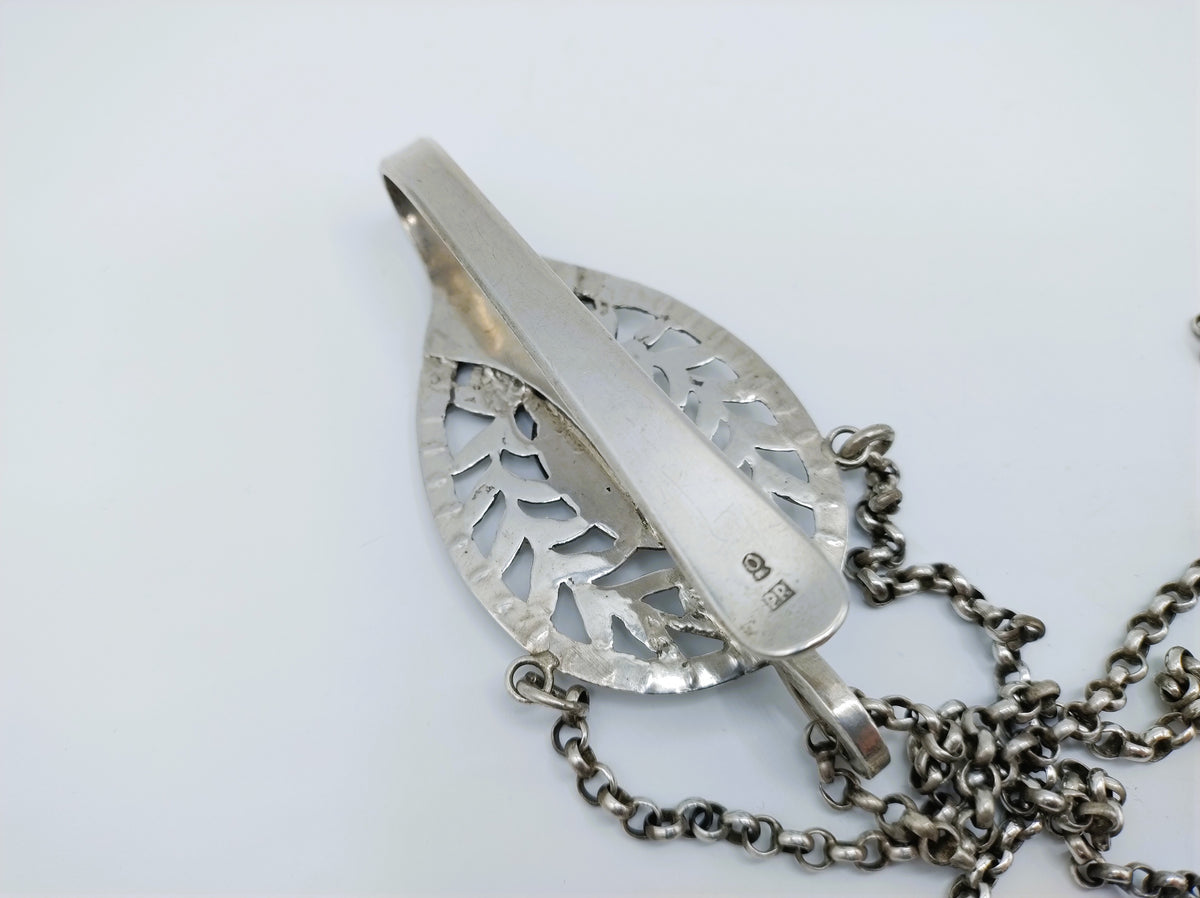 Zilveren metalen hanger met gegraveerde bladmotieven en kettinglus, close-up