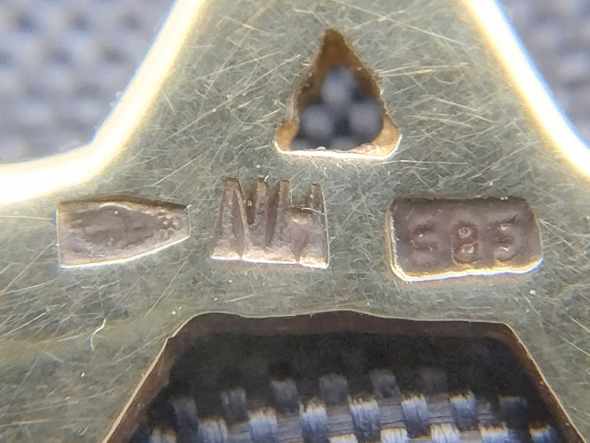 Detail van de gouden hanger met keurmerken aan de achterzijde